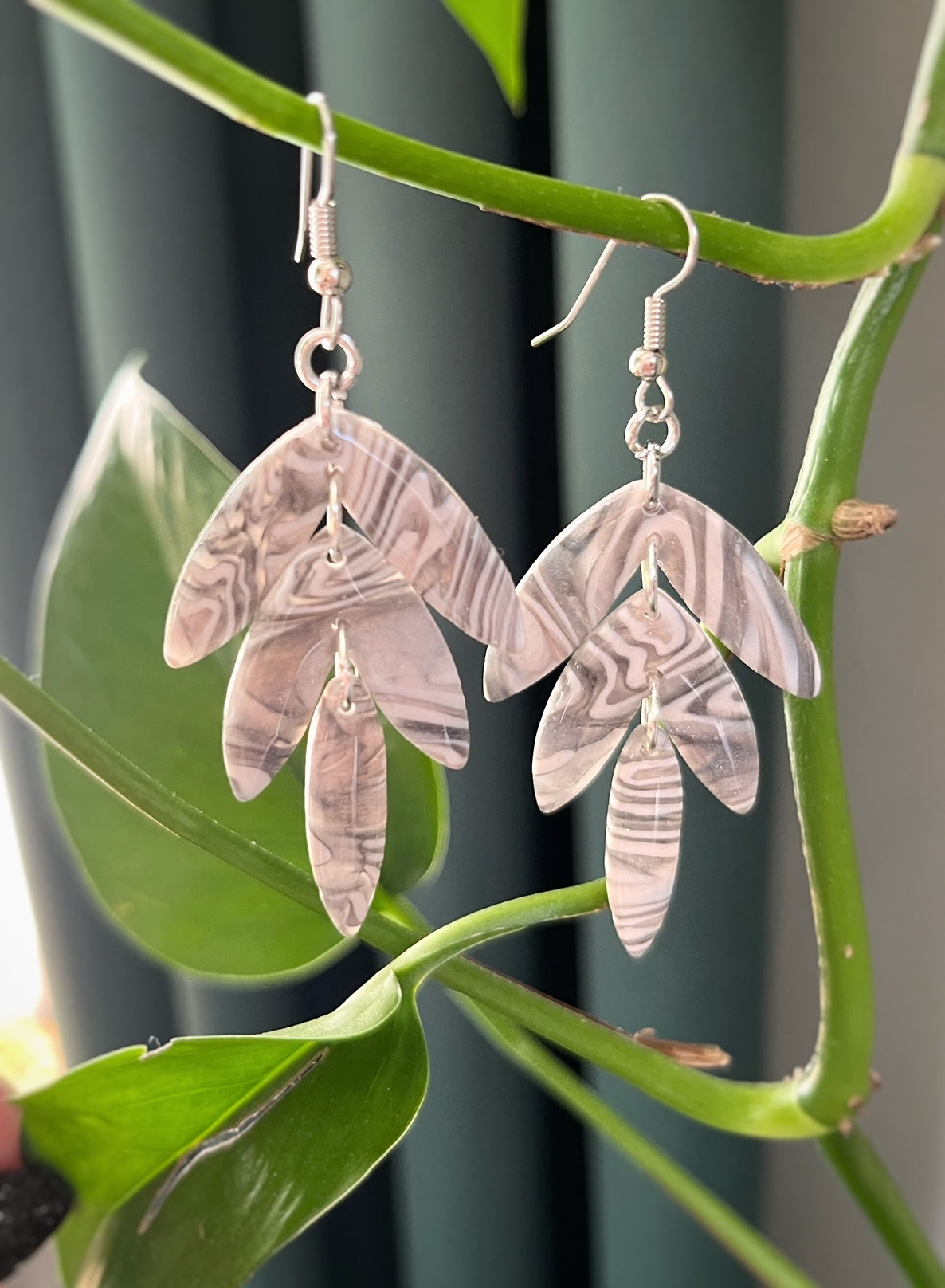 Gray leafy dangles earrings with white marble pattern hanging on plant stem
