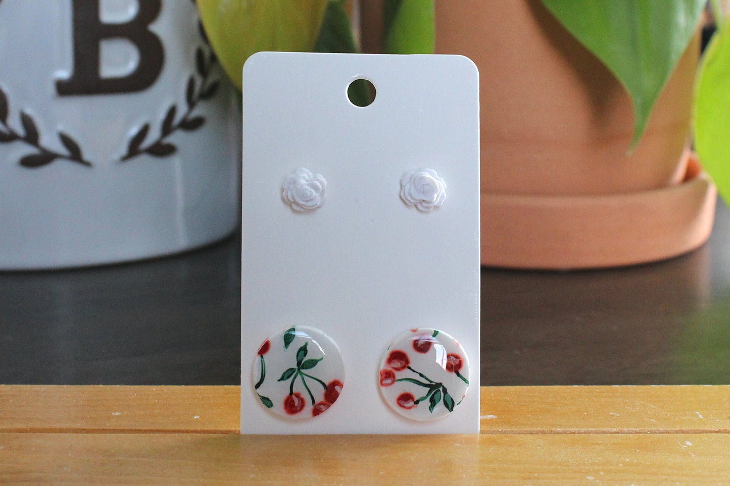 Cherry studs earrings with hand painted cherries and white rose studs on stainless steel posts displayed on a card.