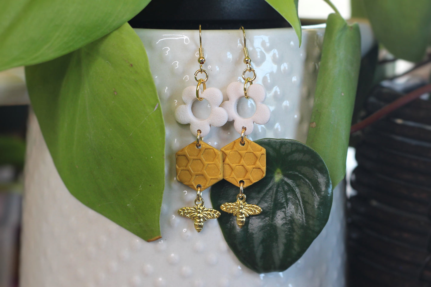 Honeycomb earrings with daisy and bee charms on nickel-free ear wires hanging on a plant pot
