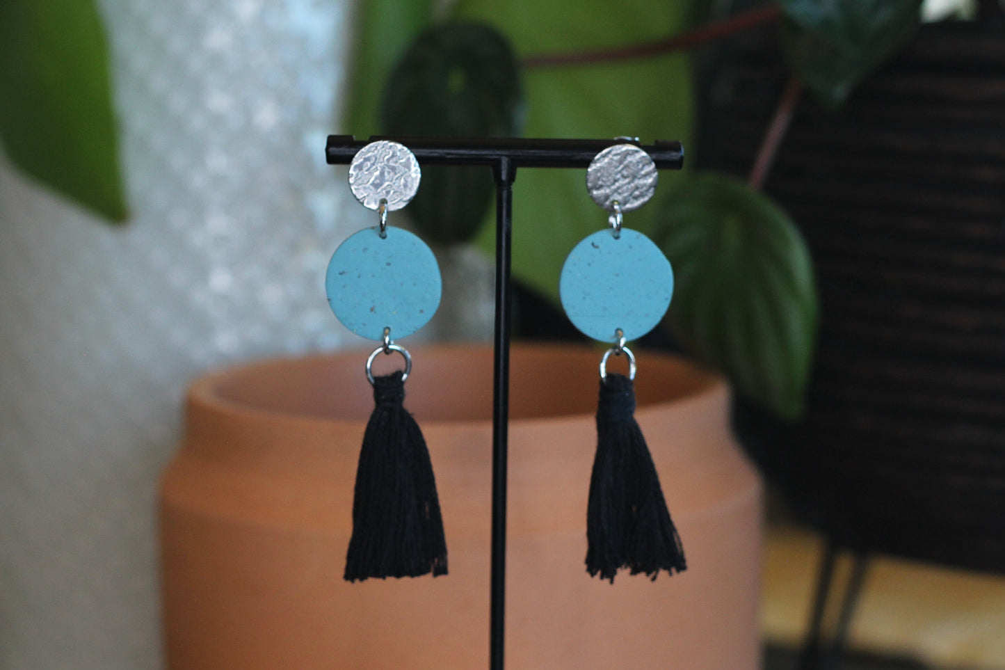 Silver stud earrings with speckled turquoise discs and black tassels hanging on a stand